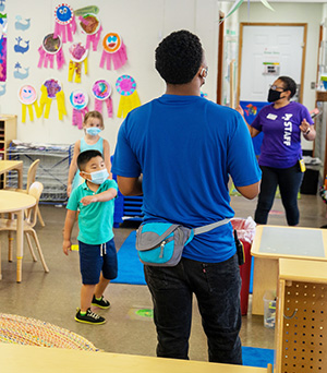 Two Y staff with two kids of preschool age wearing face coverings in a classroom