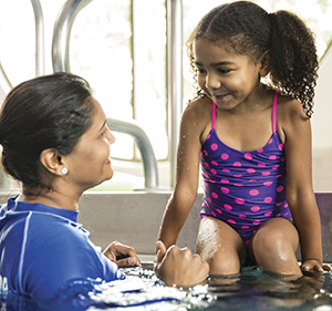 Girl sitting on the edge of the pool smiling at a swim instructor who is in the water