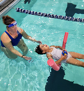 Swim instructor near a girl who is floating on her back in a pool