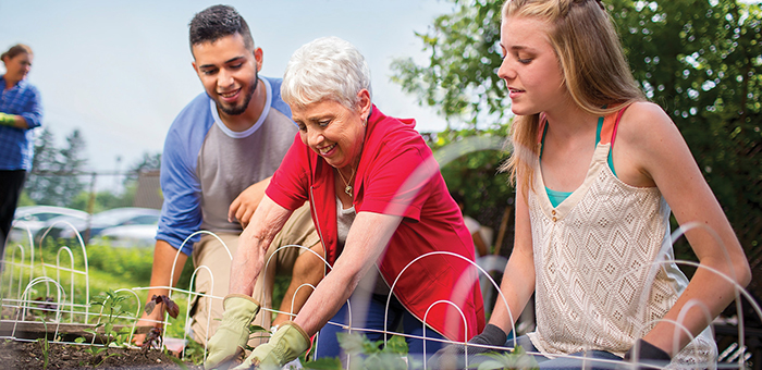 Two teens watch older woman gardening outside